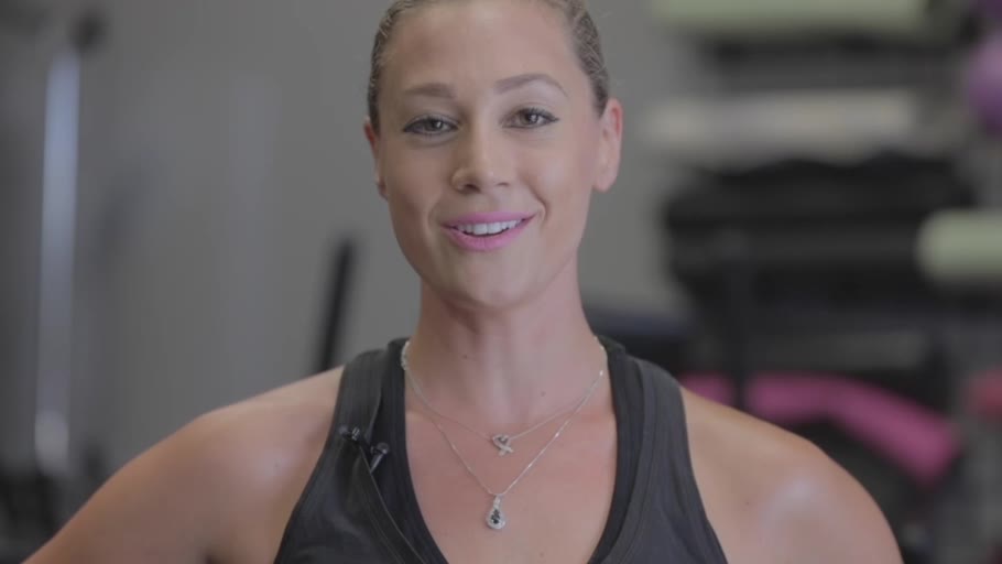 A CbK coach in the strength room, dumbbell racks behind her
