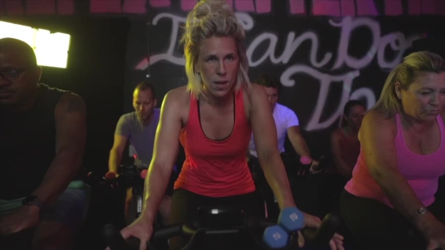 Riders holding light hand weights in the cycle room, under the “I can do this” wall